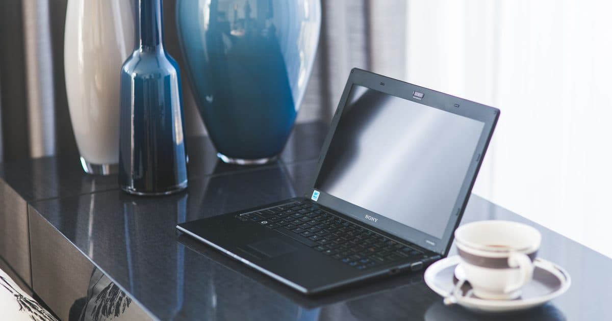 Laptop aperto su una scrivania lucida con vasi decorativi e una tazza di caffè, angolo ufficio elegante
