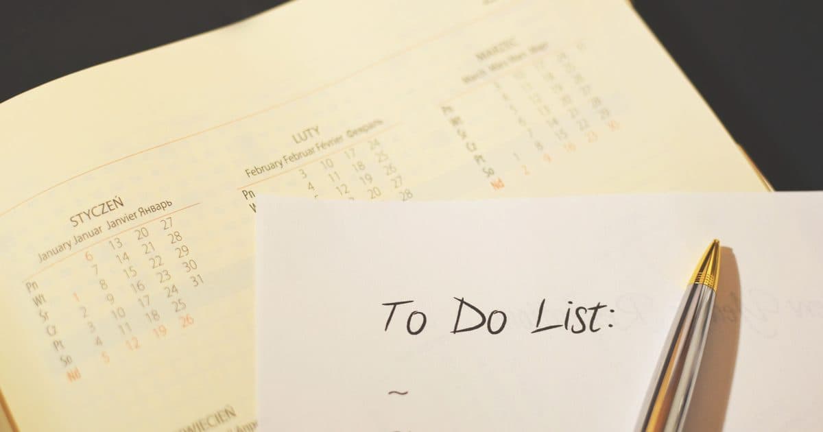Foglio con lista di cose da fare scritta a mano accanto a un calendario e una penna, primo piano